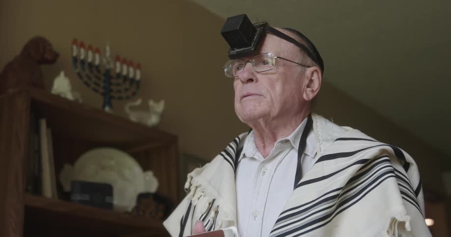 A man is standing while wearing tefillin and praying in the daytime
