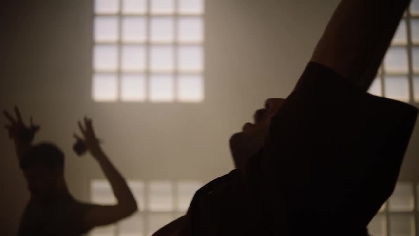 A group of people are standing in a room moving their arms in the air as they dance in unison