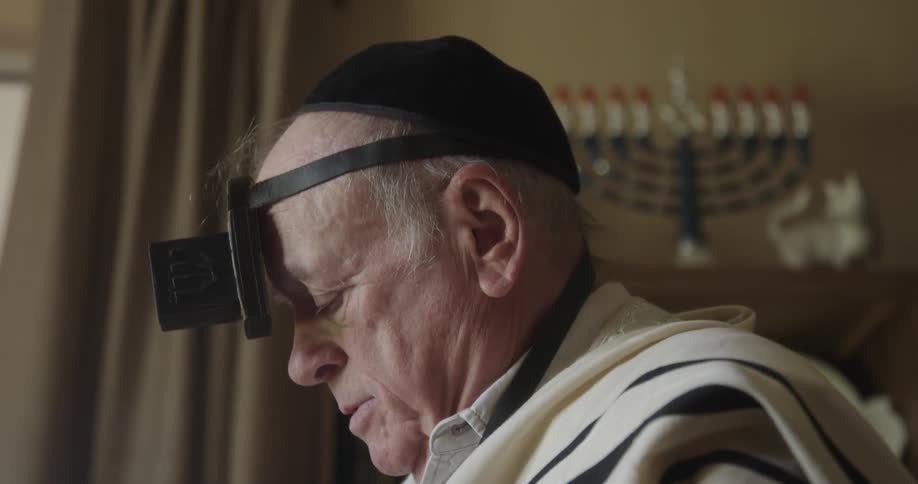 Bishop is wearing a netcap on his head and has a device on his forehead he is engrossed in reading something with his face looking down displaying a focused and concentrated expression