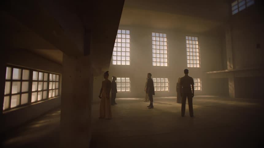 People stand stock still a distance from each other in large dimly lit empty room