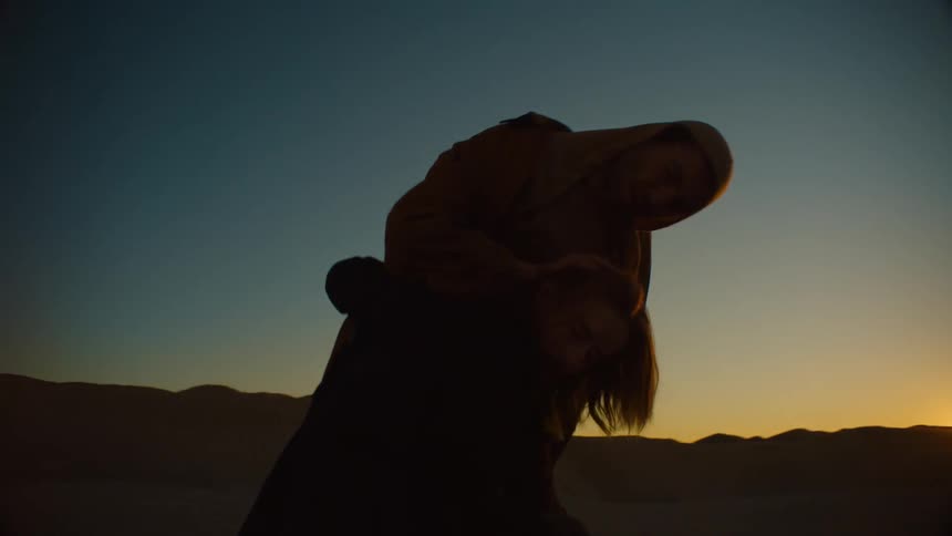 Silhouette of a couple wrapped in robes dancing in front of the sun setting in the desert