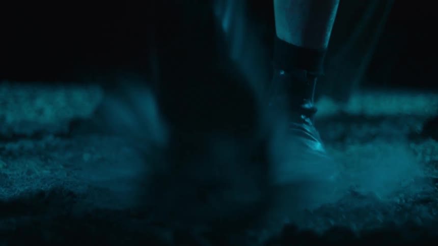 Close view of the feet of three people dancing in gravel outdoors at night