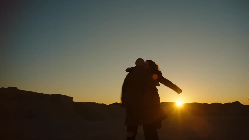 The silhouette of two people walking toward each other and hugging while the sun is setting on the horizon
