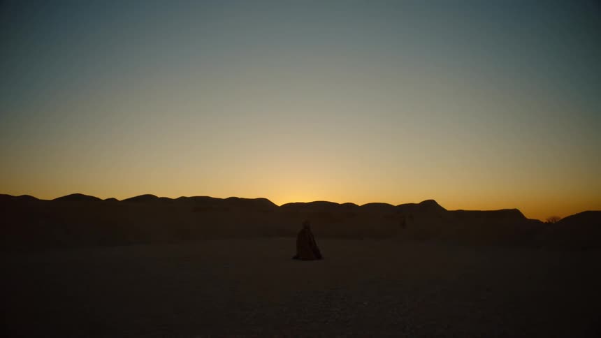 Silhouette of a man crawling on his nees on the desert at sunset