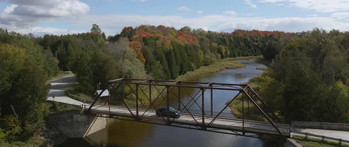 Electric vehicle driving across a bridge over a river in the countryside
