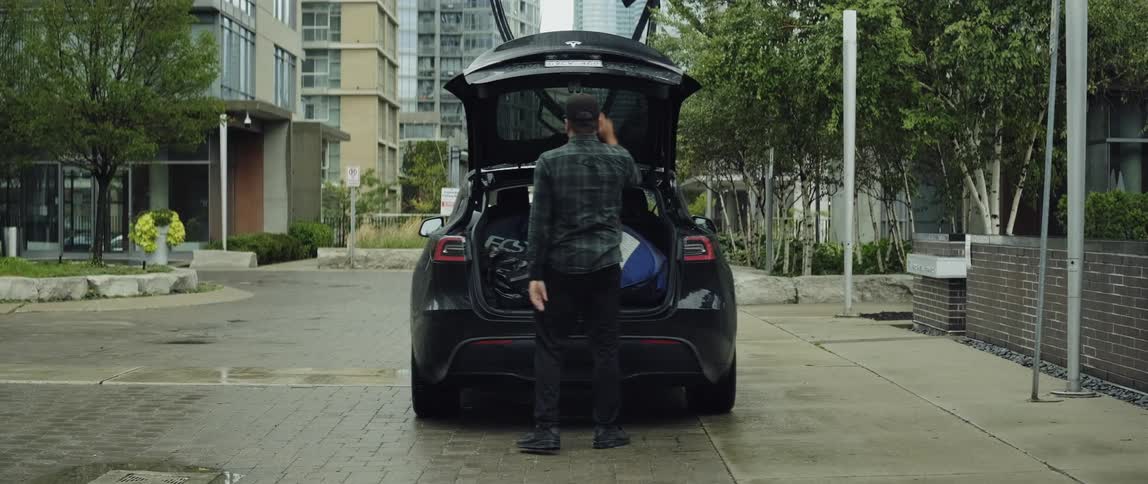A man packs bags into his electric car and closes the trunk