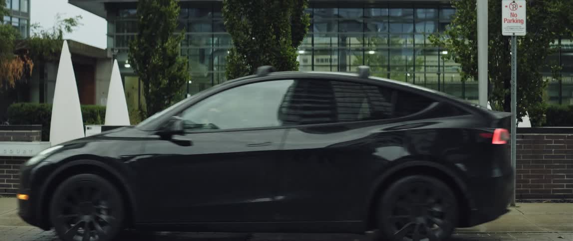 An electric car drives slowly past a modern building