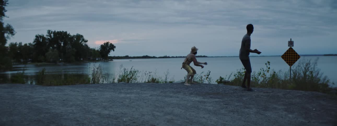 Men throw stones on shore under an overcast sky