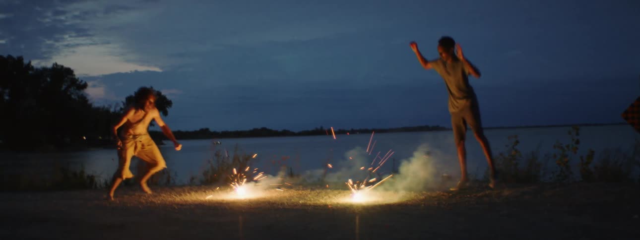 Two men jump around fireworks