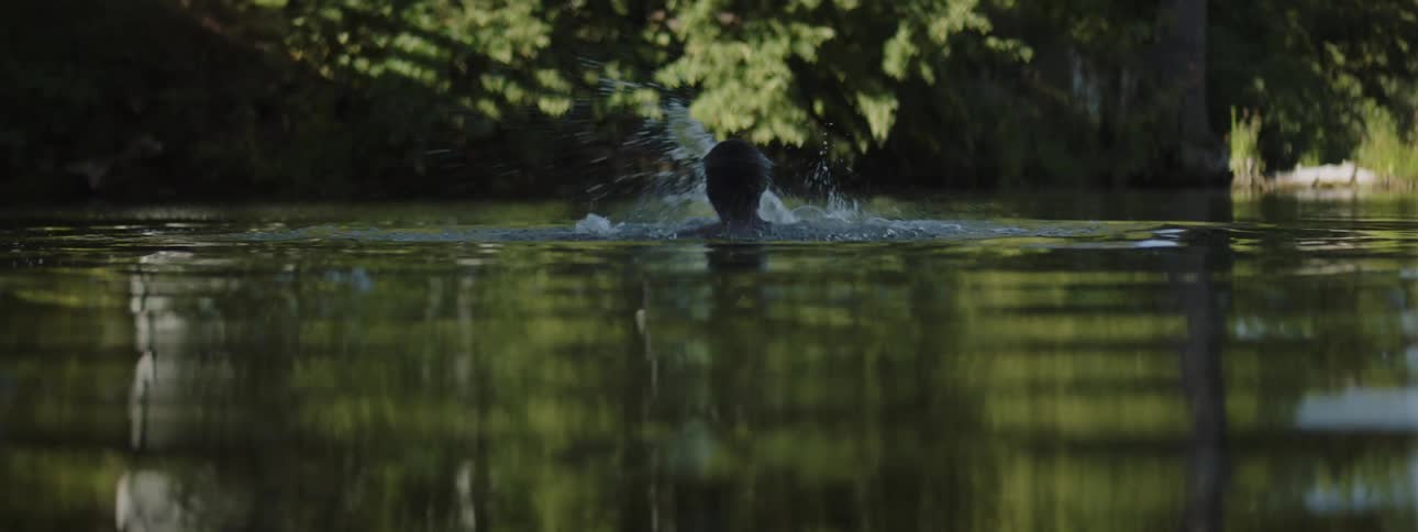 Young shirtless man swimming on a lake at daytime splashes around