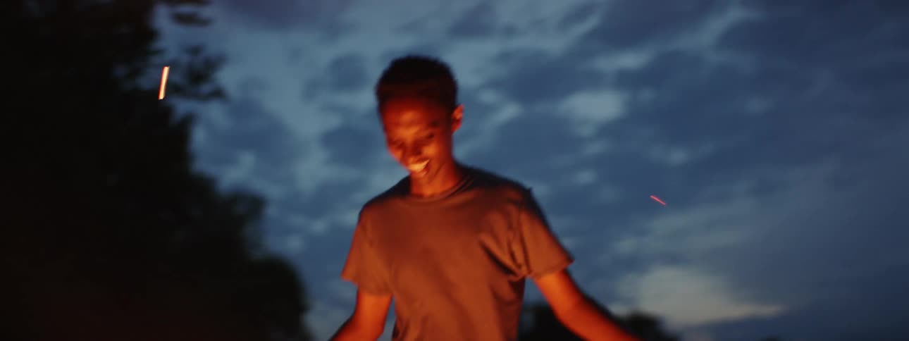 A silhouette and then full image of a young man dancing around a fire at night as the flame lights up his face
