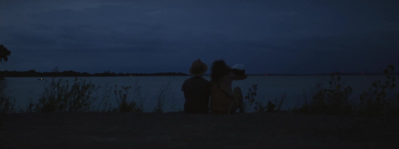 One man sits and drinks on shore with a friend as they watch lightning storm