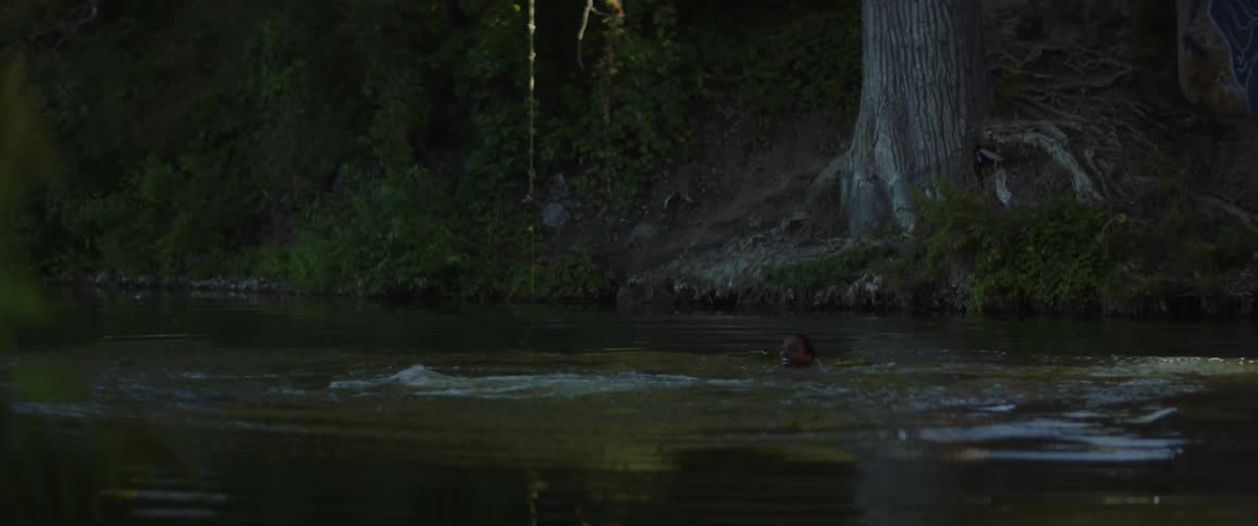 A man jumps off an bridge into a lake where another man is swimming in the daytime