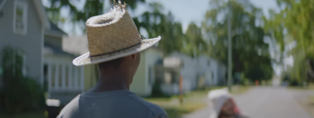 A young man is wearing a hat and walking down a neighborhood street on a sunny day