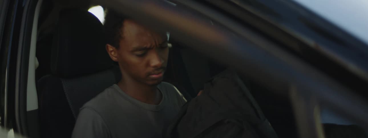 A man getting in the passenger side of a car while another man gets in the driver side and reaches for his belt