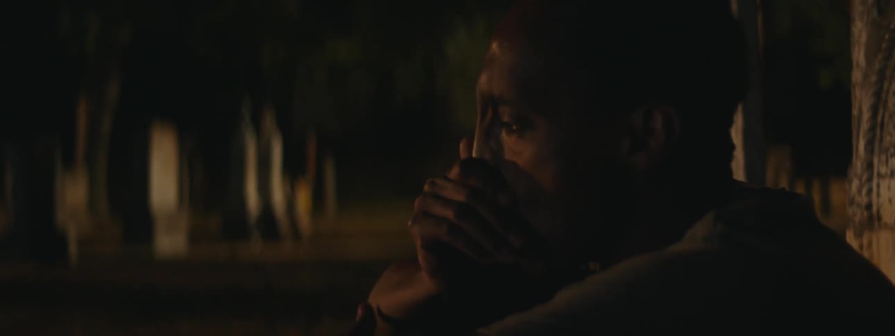 A young man is seated alone in a cemetery visibly crying overwhelmed with emotions he uses his hand to wipe away the tears from his face expressing deep sadness or distress