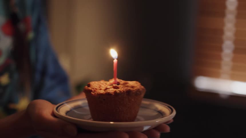 Close up of the hands of a young person carrying a cupcake with a birthday candle lit on top