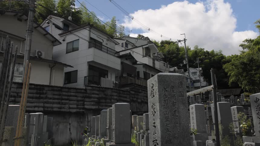 A graveyard with tall square headstones exists peacefully within a dense japanese neighborhood