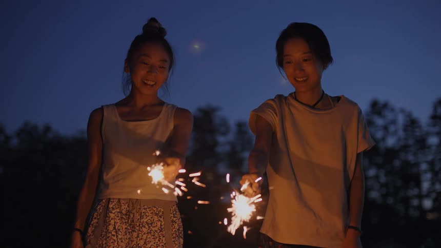 Two young women playing with sparklers in the backyard at night