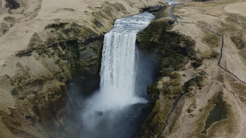 Waterfalls flow over the side of a mountain cliff as birds fly in the rising mist