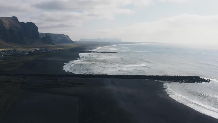 Large group of small rocks extend into ocean near town at base of cliff on foggy day