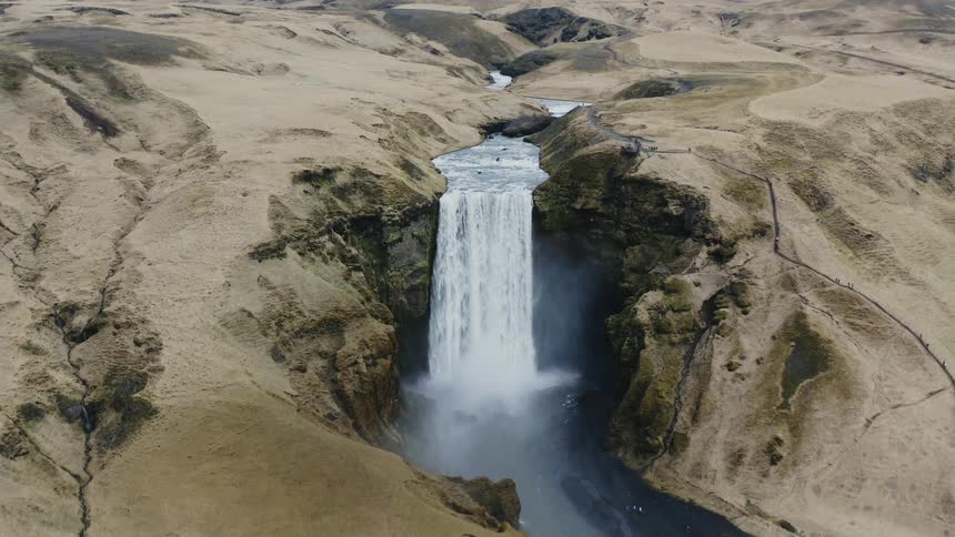 A waterfall is flowing off of a cliff in a barren wilderness area