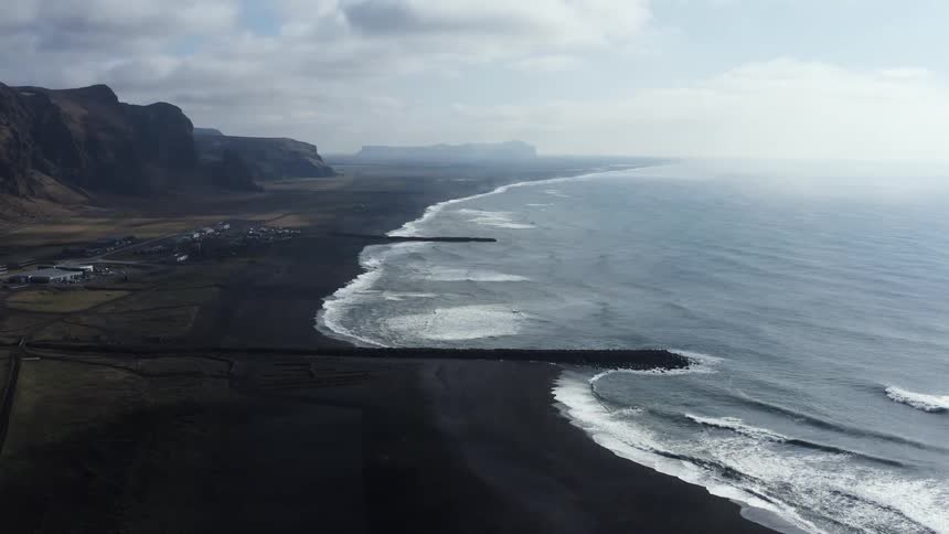 An aerial landscape view of the sea joining a northern dirt shore near some cliffs and greenery