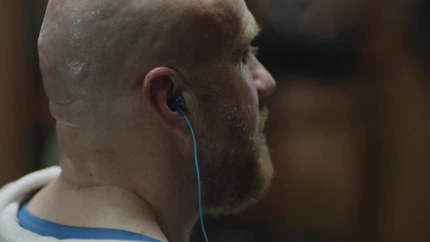 Bald man with beard takes off earphones at the gym