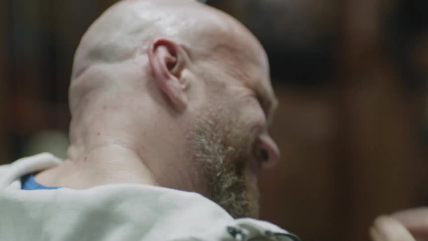 A bald man reaches back to massage his neck