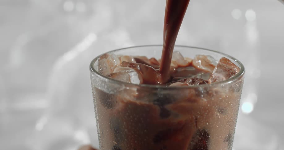 A glass filled with ice being filled with a chocolatey substance