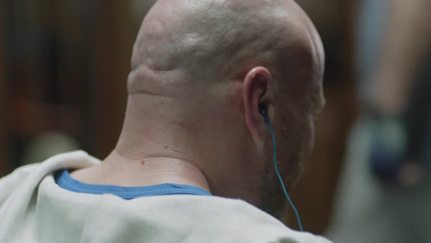 A man is in a gym and putting in earphones before leaning back