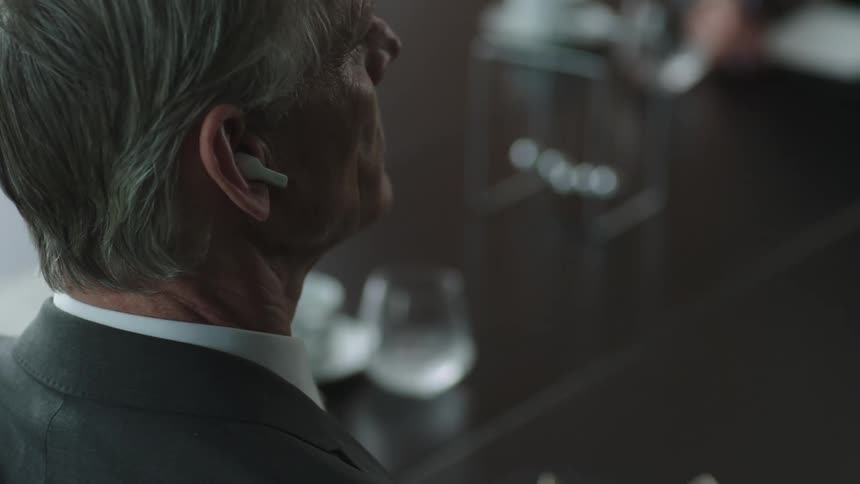 A man in a suit puts a wireless earpiece into his ear while in an office