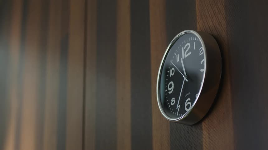 Close up of an elegant analog clock hanging from a wooden wall