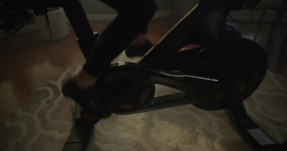 Woman with leggings and shoes rides stationary bike in the living room