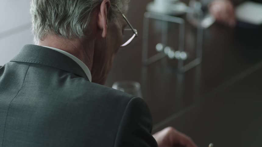 Businessman with gray hair and suit wears glasses during a business meeting