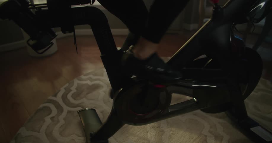 Woman with black leggings and shoes rides stationary bike in the living room