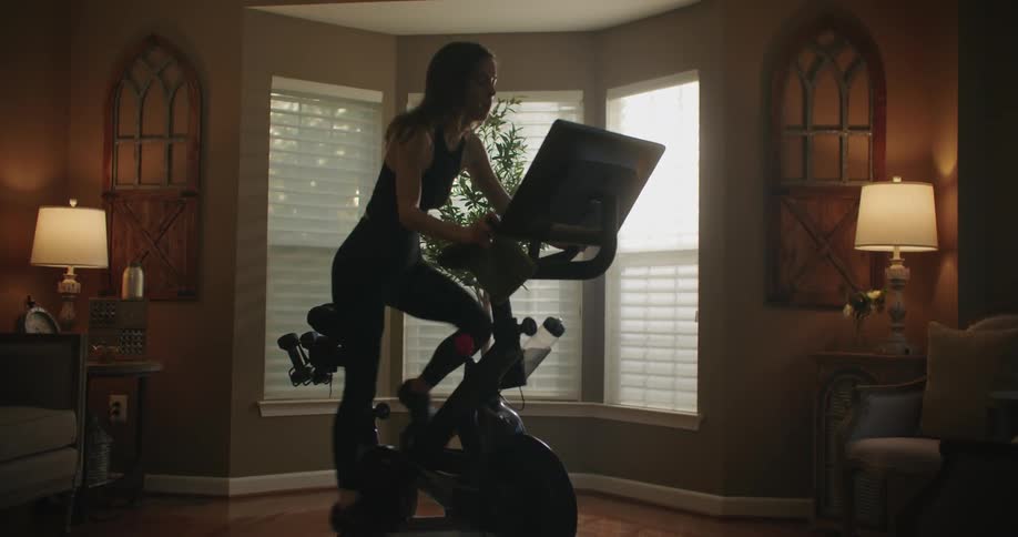 Woman with black top leggings and shoes rides stationary bike in the living room