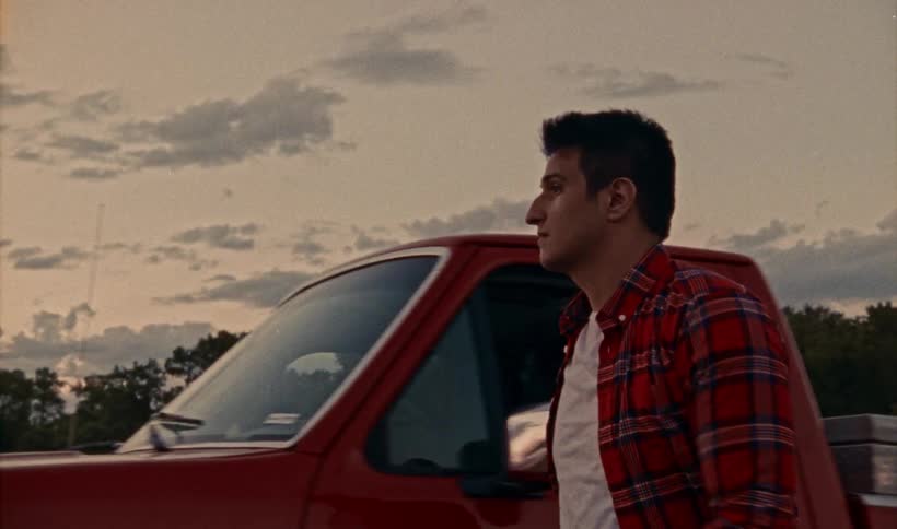 A young man getting out of a red pickup truck walking to the front and crossing his arms