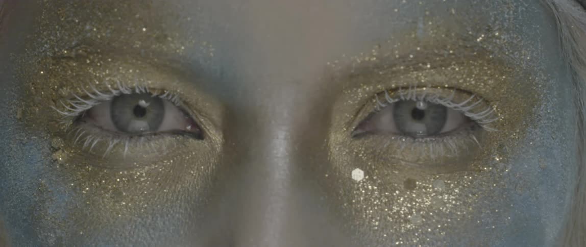 A person's eyes are covered in gold and blue glitter