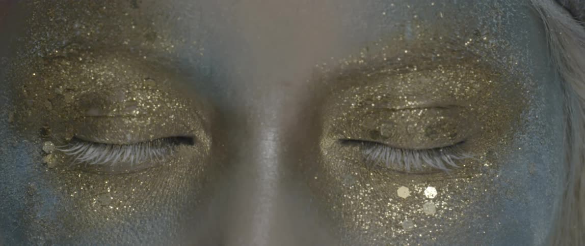A woman wearing gold glittery make up and blinking