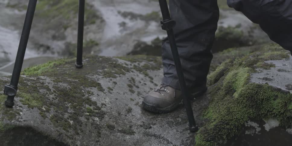 A person is standing near a tripod on some rocks