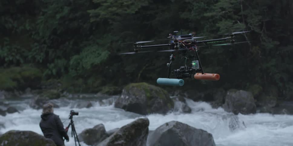 A drone is flying by a person taking photographs of a stream
