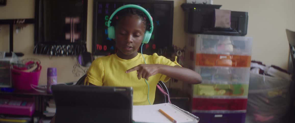 Girl wears headphones and views tablet while sitting at desk and practicing sign language