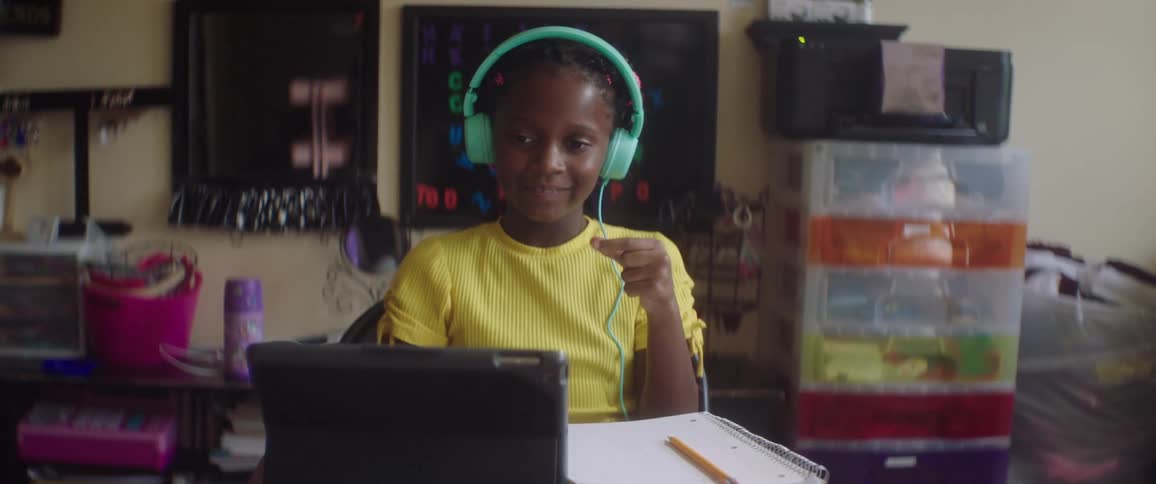 Black child with a yellow t shirt and turquoise headphones sits at the table in a room