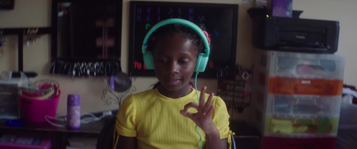 A girl sits in her room and uses a computer and headphones to learn sign language