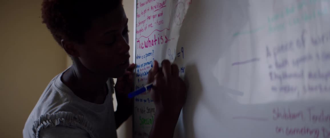 Teacher stands at white board writing as she instructs