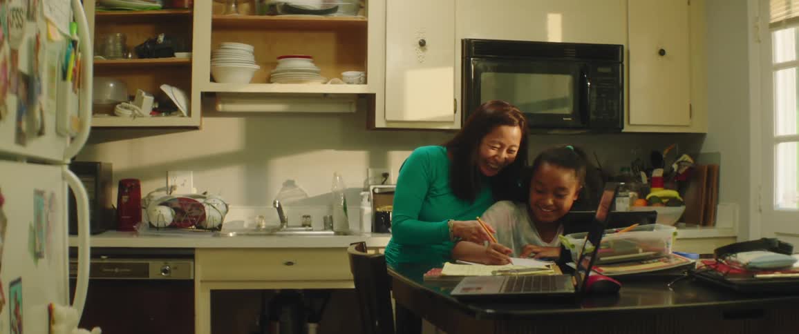 A mother laughs as she helps her daughter with homework at their kitchen table
