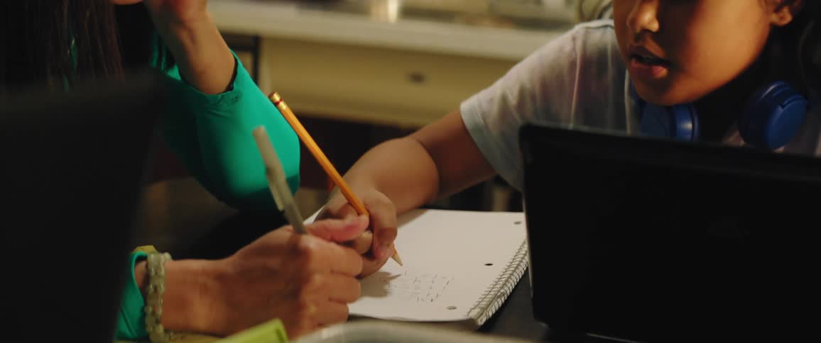 A mother helps her daughter with homework as they sit at their kitchen table