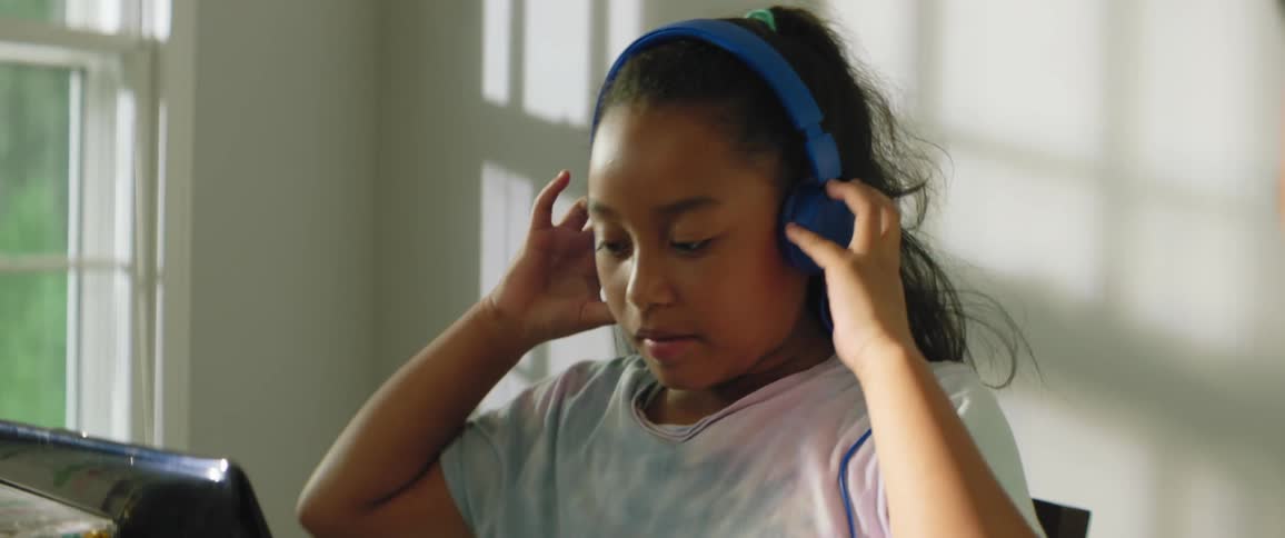 Girl dons headphones and settles down to study via her laptop