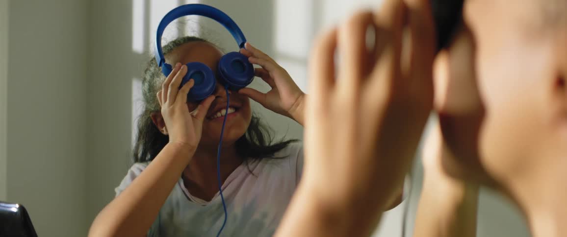 A little girl smiles as she puts her headphones over her eyes